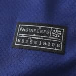 Close-up of a black label with "ENGINEERED" marked on it, stitched onto a blue Barcelona x Coldplay (Special Release) | Fan Version jersey.