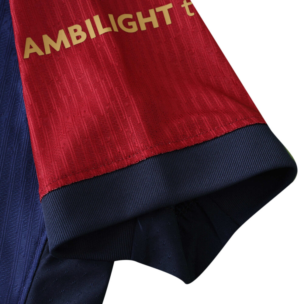 Close-up of Barcelona x Coldplay Player Version jersey sleeve, showcasing red and navy colors with gold "AMBILIGHT t" text.