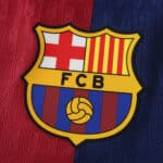 Close-up of the F.C. Barcelona crest on a striped red and blue background for the Barcelona x Coldplay (Special Release) | Player Version.