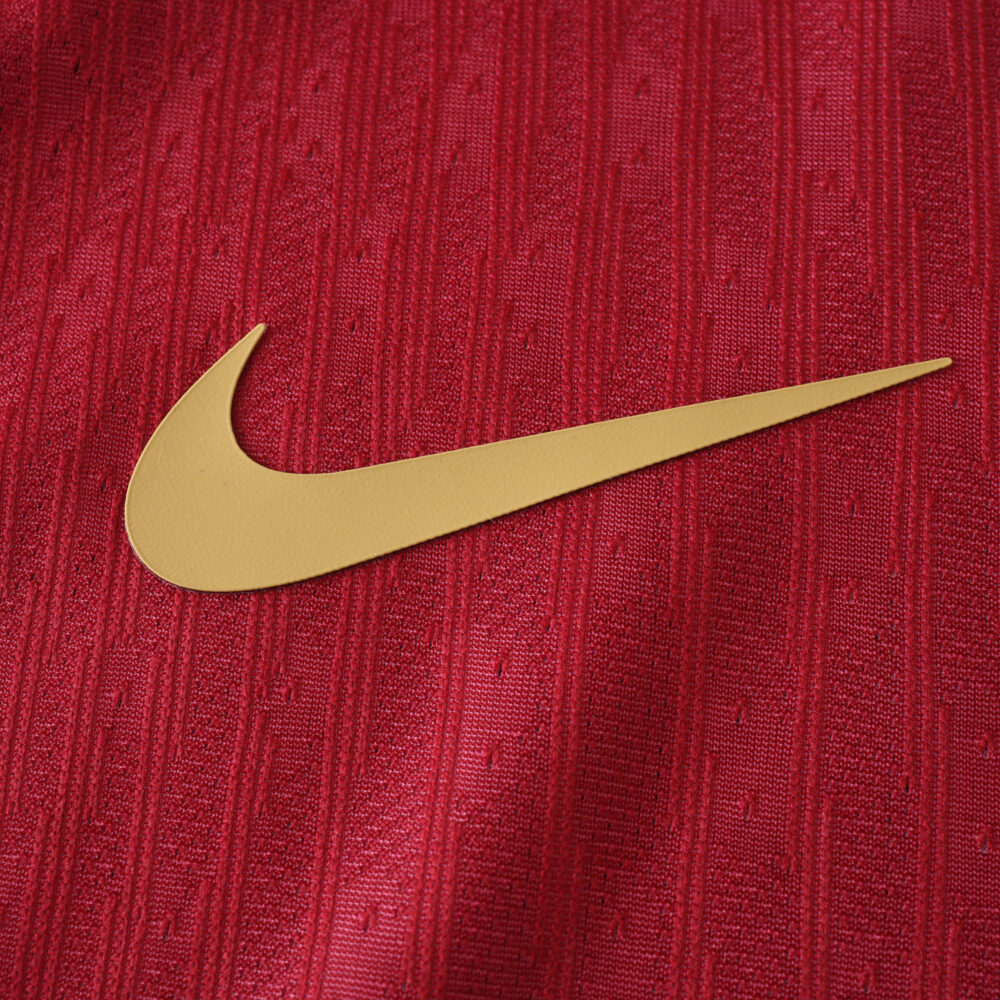 Close-up of Barcelona x Coldplay Player Version jersey featuring a gold Nike swoosh on textured red fabric.