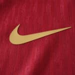 Close-up of Barcelona x Coldplay Player Version jersey featuring a gold Nike swoosh on textured red fabric.