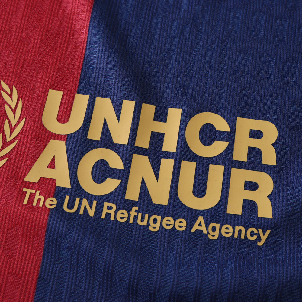 Barcelona x Coldplay (Special Release) | Player Version: Close-up of the UNHCR logo on a red and blue jersey.