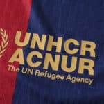 Barcelona x Coldplay (Special Release) | Player Version: Close-up of the UNHCR logo on a red and blue jersey.