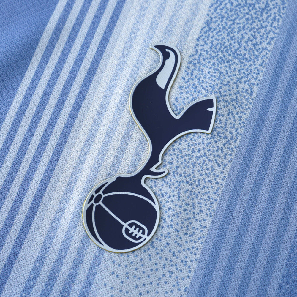 Close-up view of Tottenham x Travis Scott fan version kit displaying the team emblem on a textured grey and blue striped fabric.