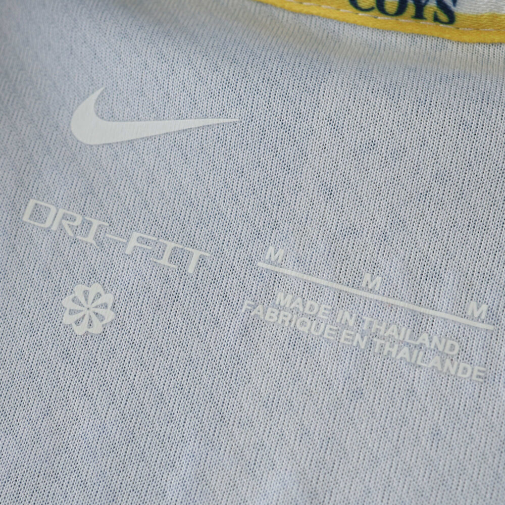 Close-up of the Tottenham x Travis Scott fan version jersey tag showing size M, Dri-Fit fabric, and "Made in Thailand."
