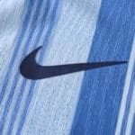 Close-up of the Nike swoosh logo on the Tottenham x Travis Scott (Special Release) Player Version jersey with blue stripes in the background.