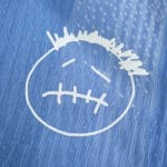 Close-up of the Tottenham x Travis Scott Player Version jersey featuring a white, stitched face graphic on blue fabric.
