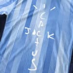 Tottenham x Travis Scott Player Version jersey close-up showing "CACTUS JACK" text in white on a blue striped background.