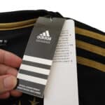 Close-up of a hand holding the tags of the Juventus Retro Third 2015/16 jersey, highlighting Adidas branding and official product details.