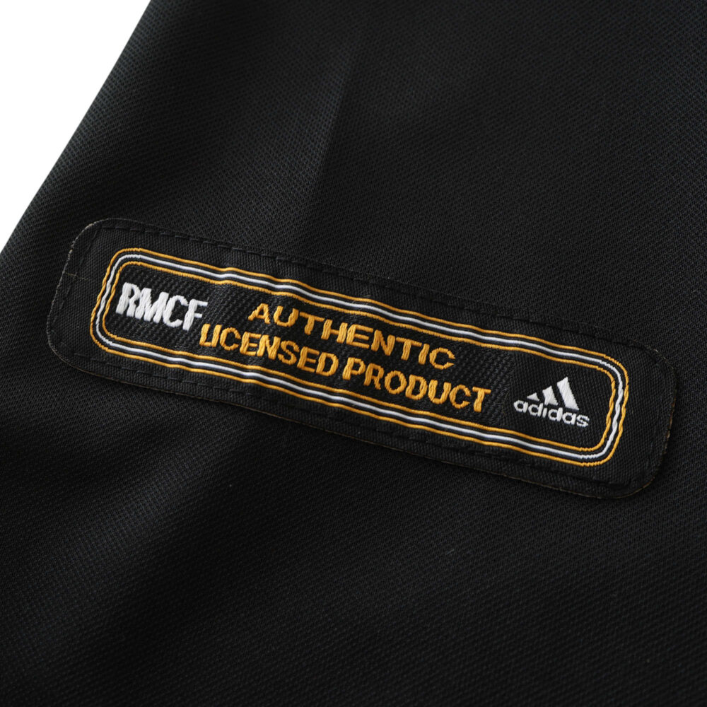 Close-up of the official "Real Madrid Authentic Licensed Product" label on a black retro away jersey for the 2001/02 season.