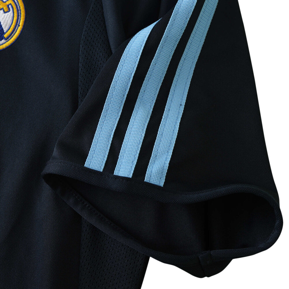 Close-up of the sleeve of Real Madrid Retro Away 2003/04 Fan Version jersey, showcasing light blue stripes and part of the club logo.