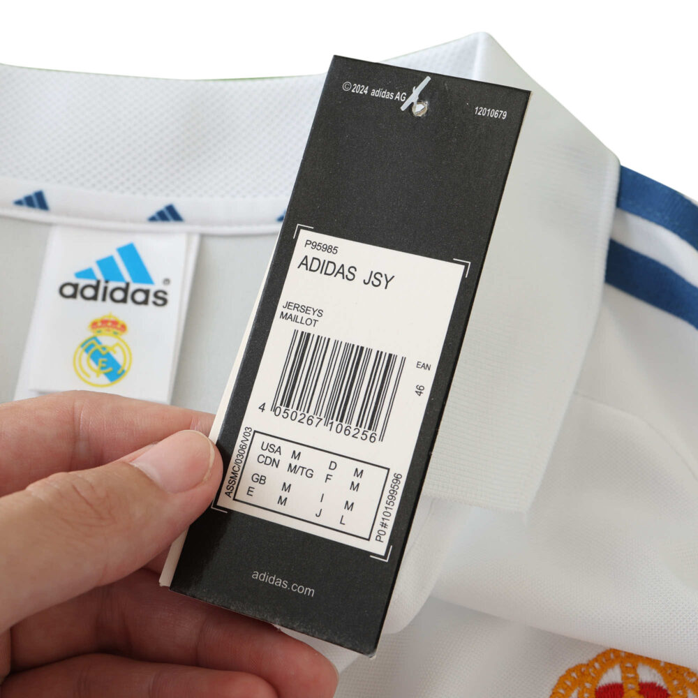A close-up of a hand holding the tag of the Real Madrid Retro Home 2001/02 Fan Version jersey, displaying product and size details.