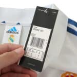 A close-up of a hand holding the tag of the Real Madrid Retro Home 2001/02 Fan Version jersey, displaying product and size details.