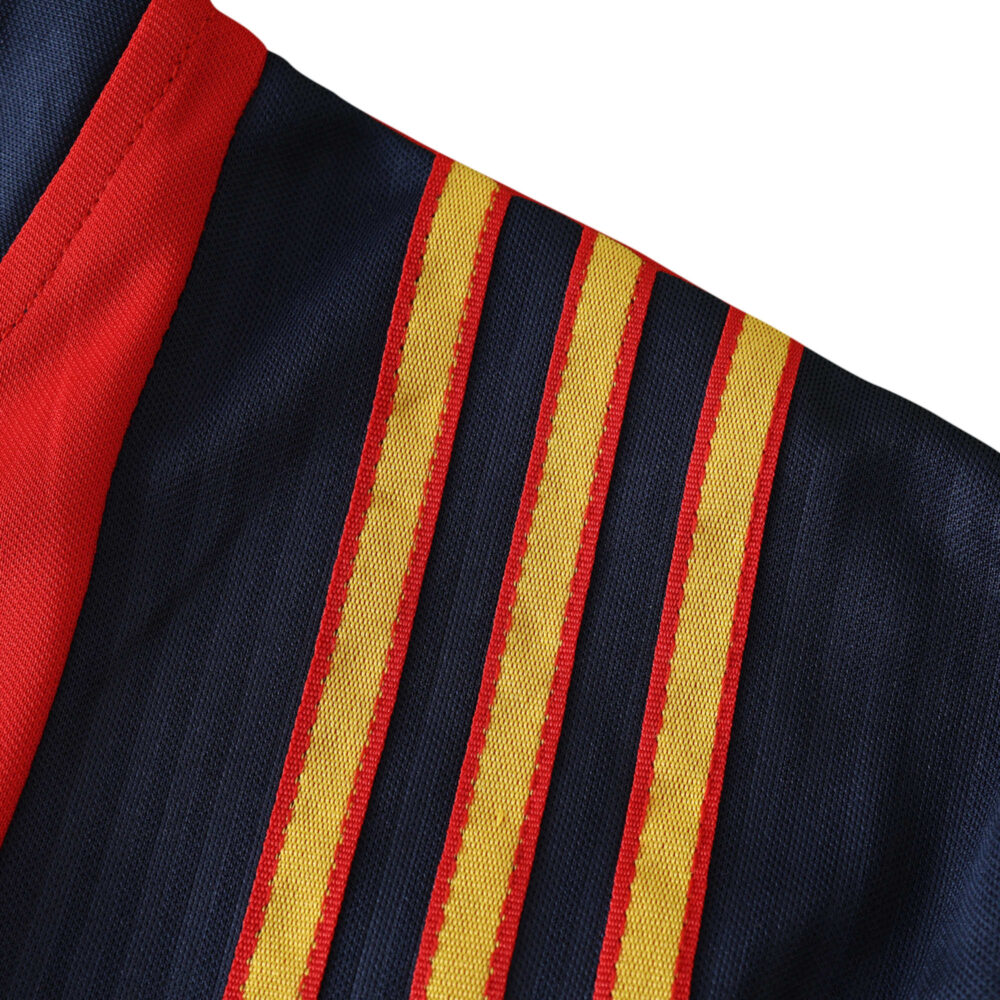 Close-up of Spain Retro Home 1996 Fan Version jersey showcasing red and yellow shoulder stripes on a dark blue background.