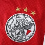 Ajax Home 2025/26 Fan Version jersey badge with club crest and three gold stars on red fabric.