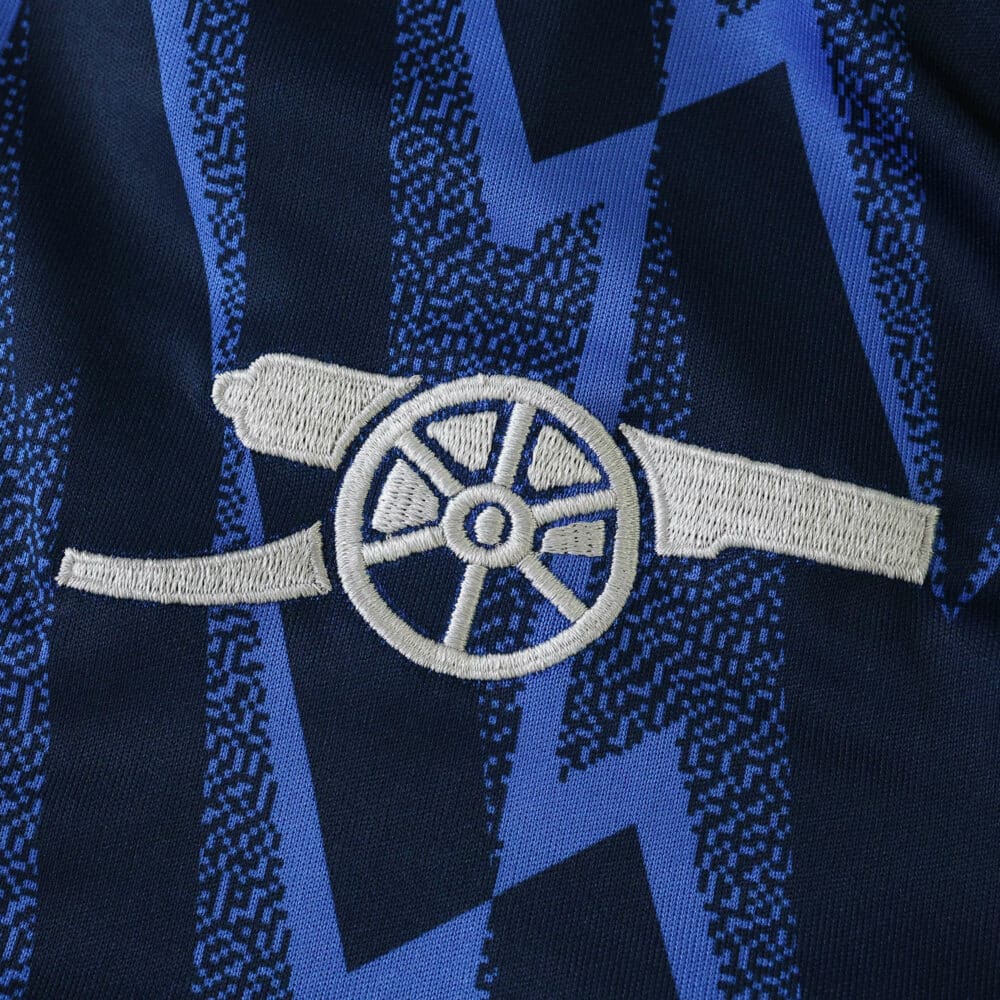 Close-up of Arsenal away 2025/26 fan jersey featuring the club’s cannon crest on a blue patterned fabric.