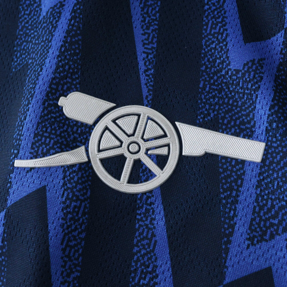 Close-up of the Arsenal cannon crest on the 2025/26 Away Player Version jersey with blue geometric patterns.