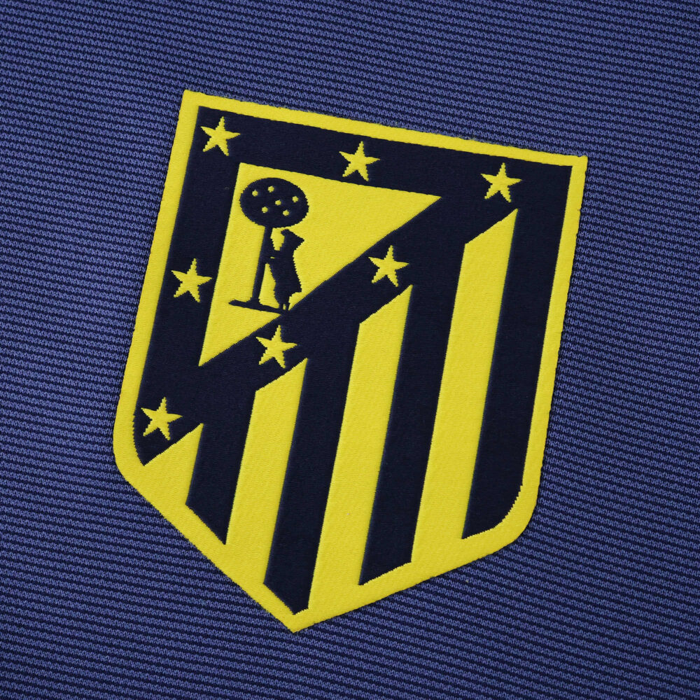 Close-up of the Atlético Madrid 2025/26 away fan version badge on blue fabric.