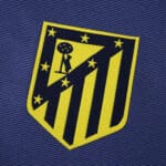 Close-up of the Atlético Madrid 2025/26 away fan version badge on blue fabric.