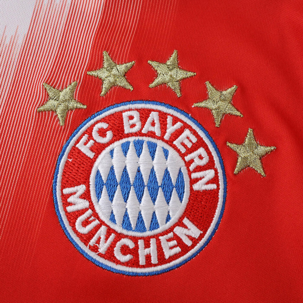 Close-up of the Bayern Munich crest with four gold stars on the 2025/26 home fan jersey.