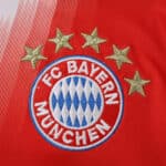 Close-up of the Bayern Munich crest with four gold stars on the 2025/26 home fan jersey.