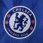 Close-up of the Chelsea FC crest on the 2025/26 fan version home jersey in blue.