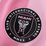 Close-up of the Inter Miami CF home 2025/26 player version jersey badge on pink fabric.