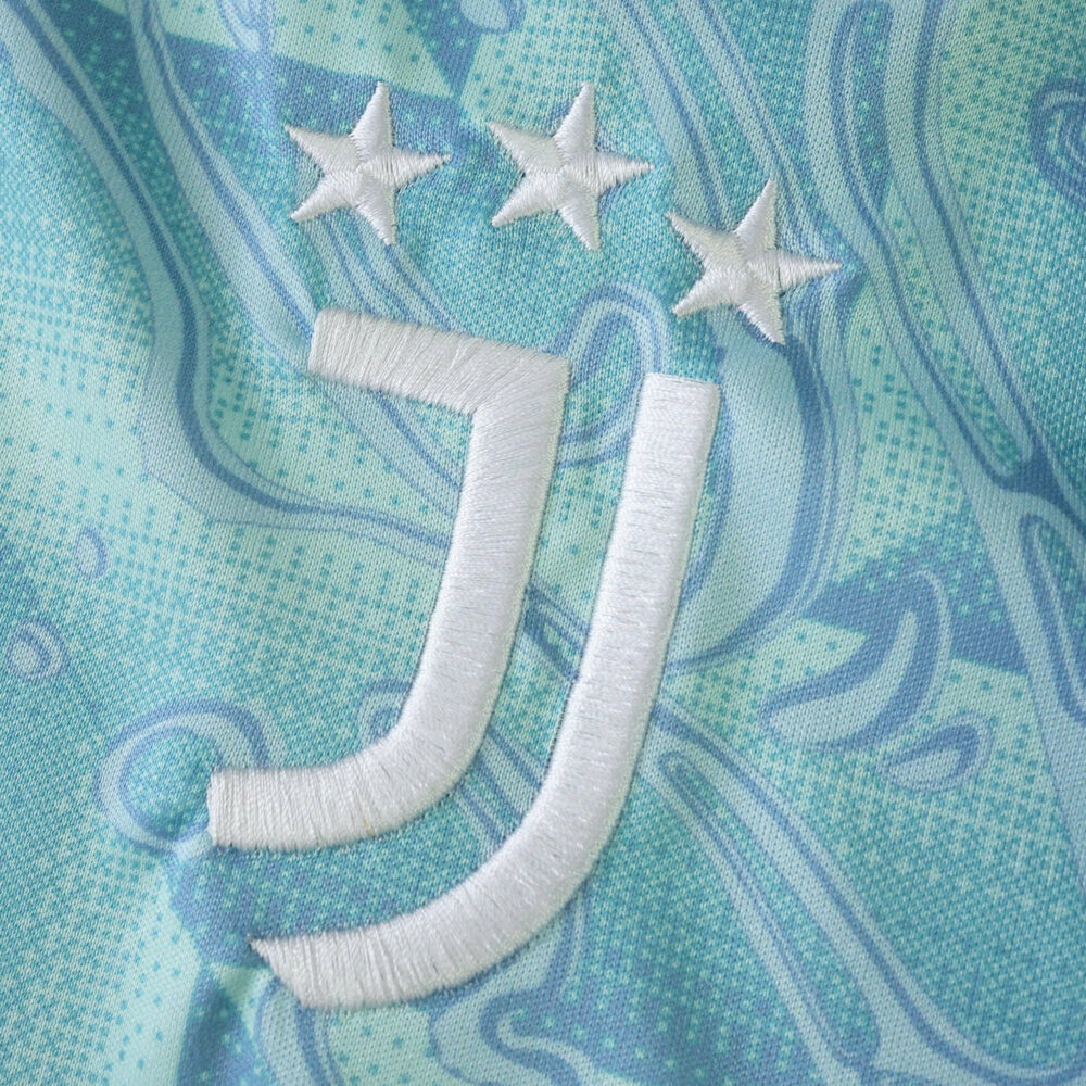 Close-up of Juventus 2025/26 Away Fan Version jersey with club logo and three stars on aqua patterned fabric.