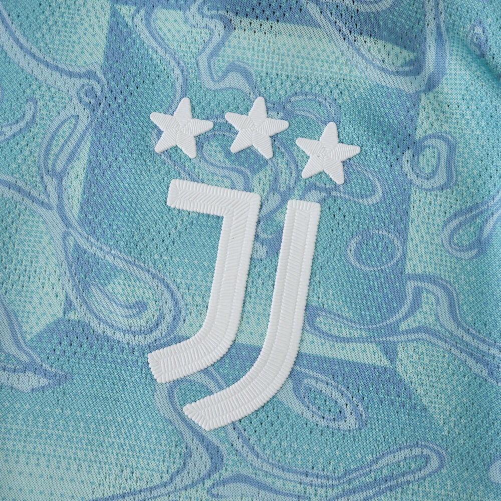 Close-up of the Juventus 2025/26 away jersey badge with three stars on blue patterned fabric.