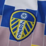 Leeds United 2025/26 home fan jersey featuring the LUFC crest on a blue, white, and gold patterned fabric.