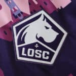 Close-up of the Lille LOSC crest on the 2025/26 Away Fan Version jersey with a pink graphic background.