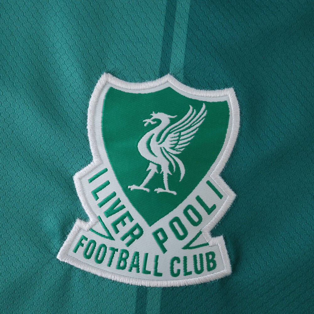 Close-up of the Liverpool Third 2025/26 Fan Version crest on a green football jersey.