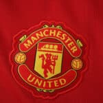 Manchester United crest embroidered on the red 2025/26 home fan version jersey fabric.