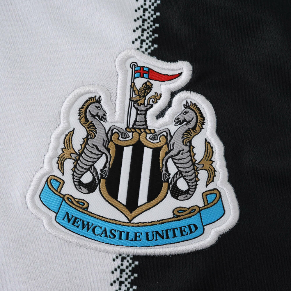 Newcastle United crest on the 2025/26 home fan version jersey, white and black fabric background.