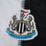 Newcastle United crest on the 2025/26 home fan version jersey, white and black fabric background.