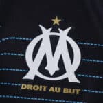 Olympique Marseille away jersey 2025/26 fan version crest with gold star and "Droit Au But" text.