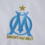 Olympique Marseille crest with gold star and "Droit Au But" on the 2025/26 home fan version jersey.