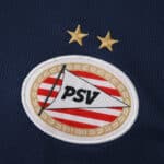 Close-up of the PSV Eindhoven 2025/26 away fan jersey badge with two gold stars above the crest.