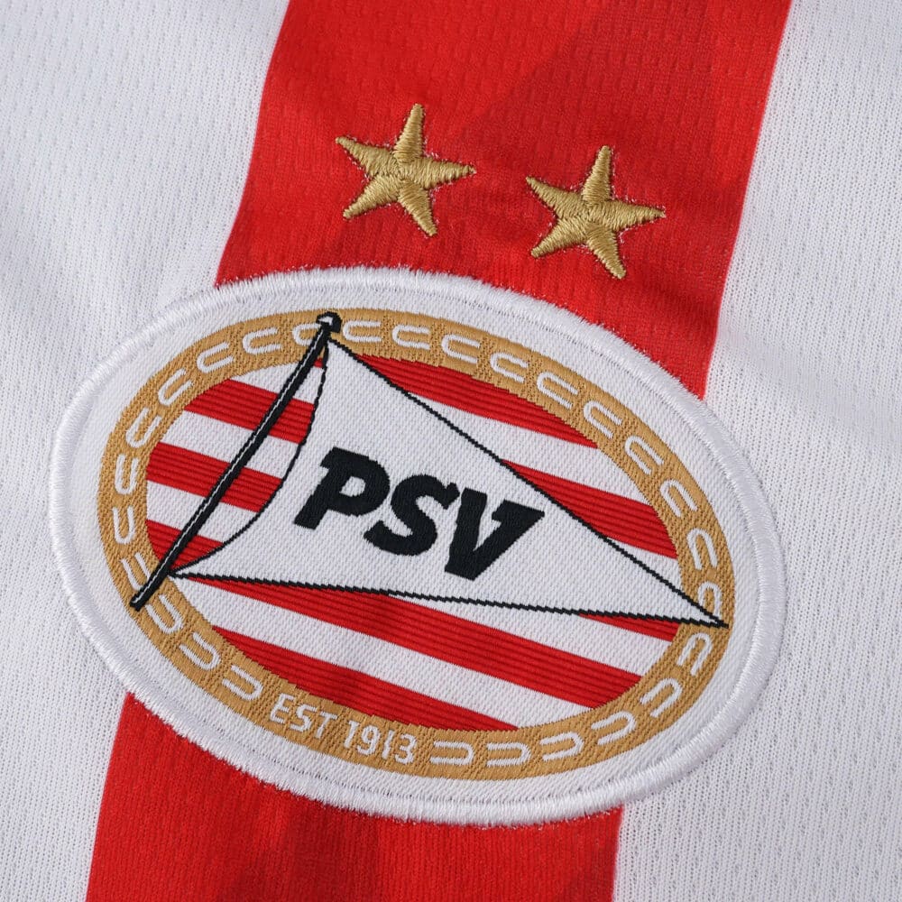 Close-up of the PSV Eindhoven 2025/26 Home Fan Version jersey badge with two gold stars above the crest.