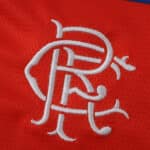 White Rangers FC crest embroidered on red fabric, featured on the 2025/26 away fan version jersey.