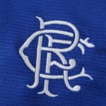 Close-up of the white Rangers FC crest embroidered on blue fabric, 2025/26 Home Fan Version jersey.