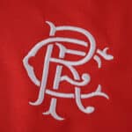 White Rangers crest embroidered on red fabric, featured on the 2025/26 Third Fan Version jersey.