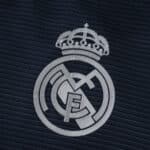 Close-up of the Real Madrid crest on the 2025/26 Away Player Version jersey, navy blue background.
