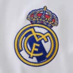 Embroidered Real Madrid crest on white fabric, featured on the 2025/26 home fan jersey.