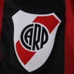 Close-up of the River Plate crest on the 2025/26 away fan version jersey with black and red stripes.