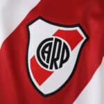 Close-up of the River Plate 2025/26 home jersey badge, featuring the club crest on red and white fabric.