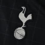 Close-up of the Tottenham Hotspur crest on the 2025/26 away fan jersey, featuring a dark grid pattern.