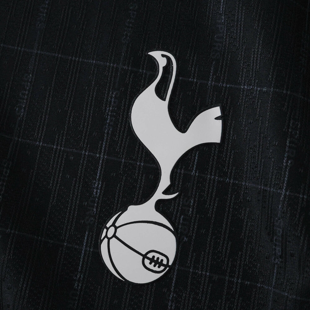 Tottenham Hotspur crest on the 2025/26 away player version jersey, black background with subtle patterns.