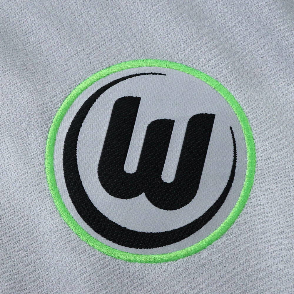 Close-up of the VfL Wolfsburg logo on the 2025/26 away fan version jersey.