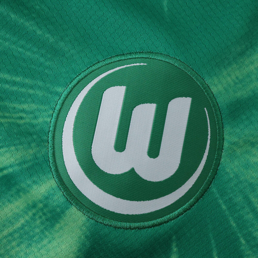 Close-up of the VfL Wolfsburg home jersey 2025/26 fan version, showing the embroidered club crest.